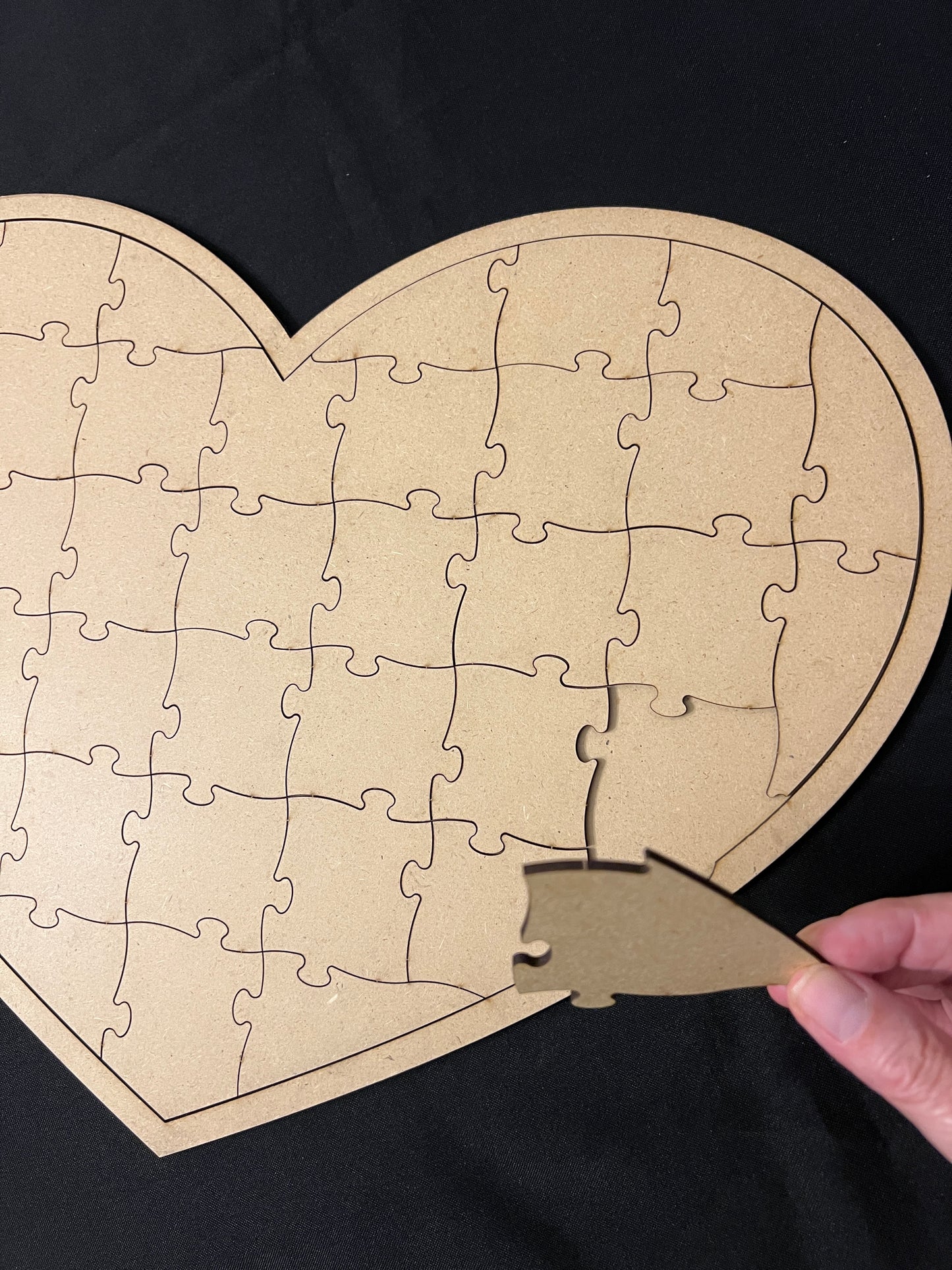 Heart-shaped cardboard puzzle with a hand holding a piece against a black background