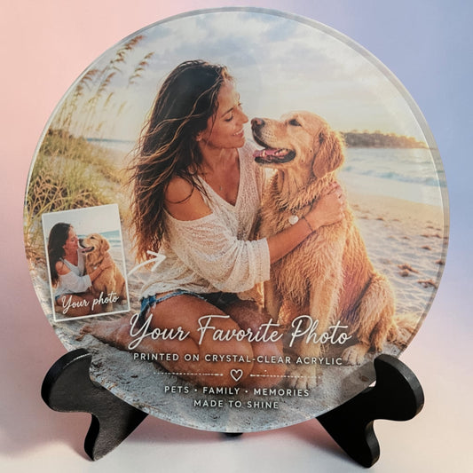 A round custom photo acrylic plate displayed on a black stand, featuring a printed image of a woman and her golden retriever on a beach. The plate includes customizable text reading 'Your Favorite Photo' and product details at the bottom.