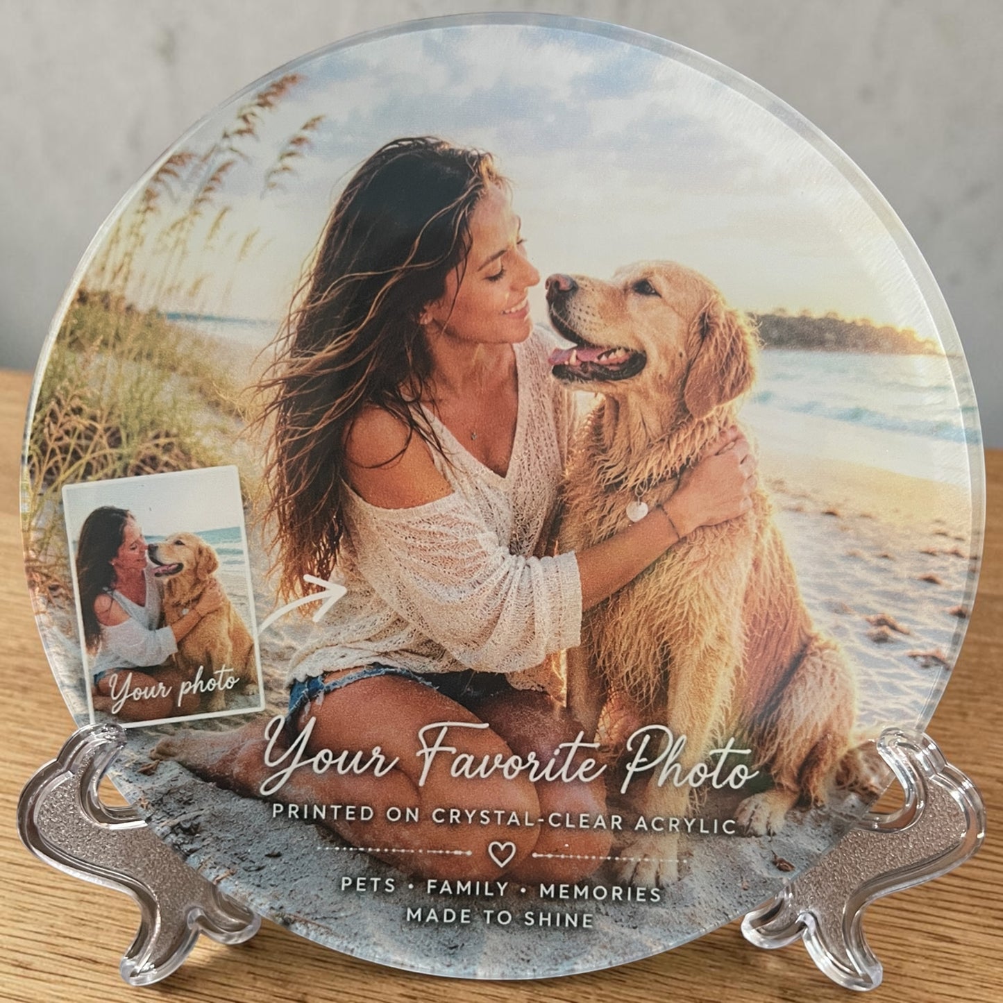 A round custom photo print on clear acrylic displayed on a silver stand. The printed design shows a woman hugging a golden retriever at the beach, with text reading 'Your Favorite Photo' and 'Printed on crystal clear acrylic.