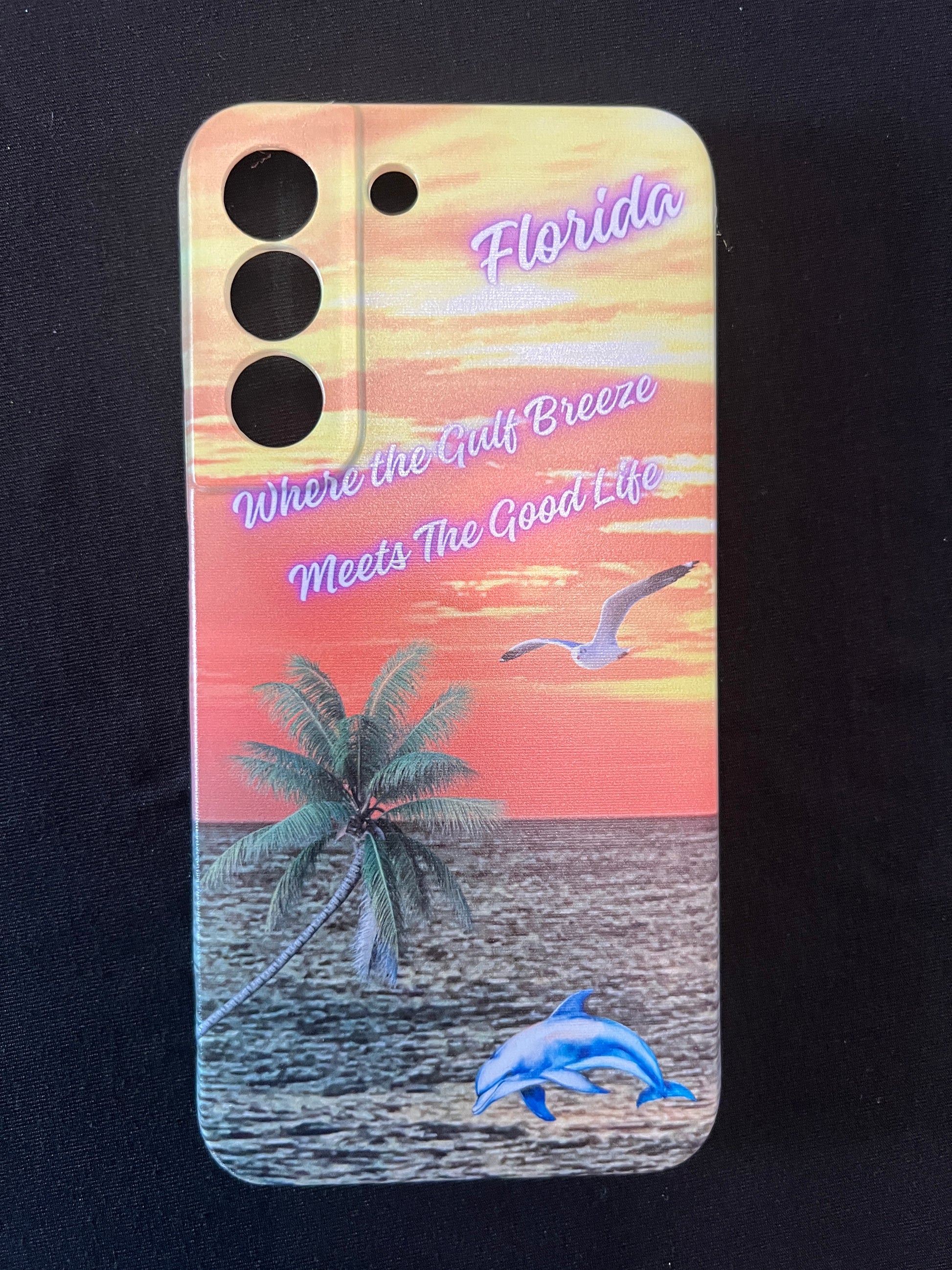 Phone case with Florida design featuring palm tree, dolphin jumping out of the water, seagull jumping out of the gulf water, beautiful Florida sunset, and text with the phrase "where the gulf breeze meets the good like" Florida