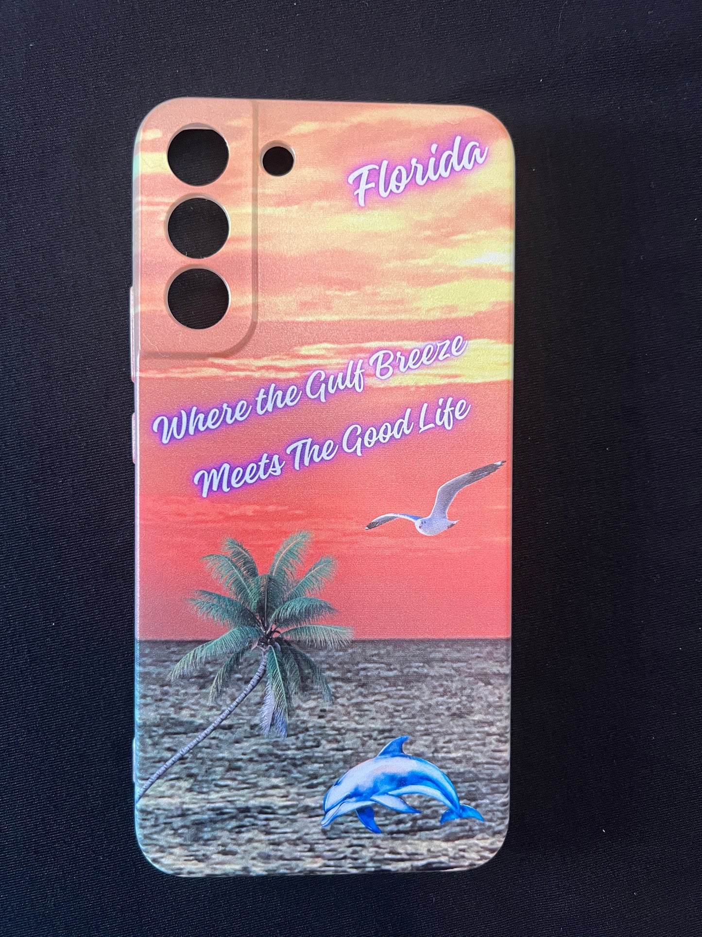 Phone case with Florida design featuring palm tree, dolphin jumping out of the water, seagull jumping out of the gulf water, beautiful Florida sunset, and text with the phrase "where the gulf breeze meets the good like" Florida