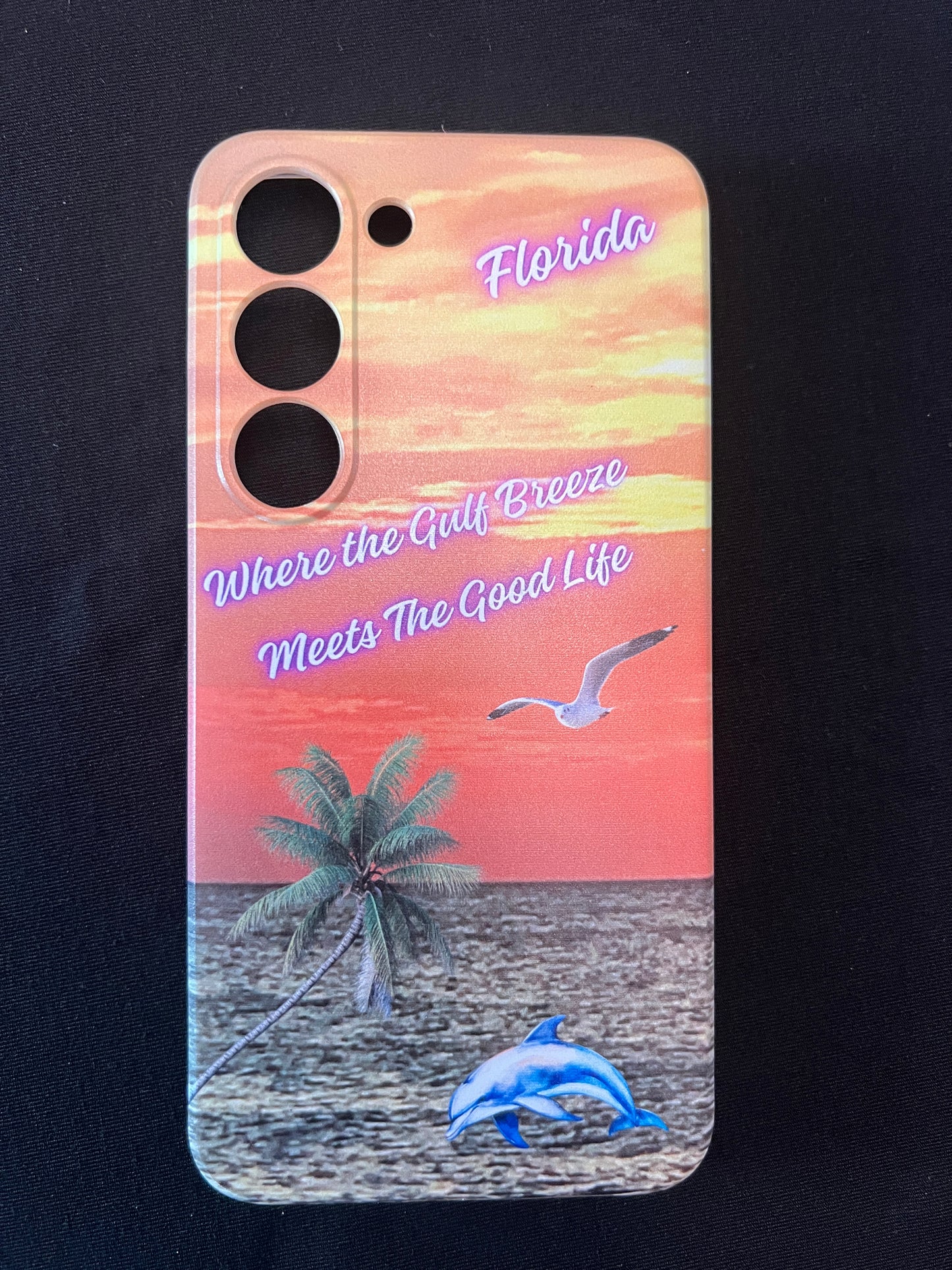 Phone case with Florida design featuring palm tree, dolphin jumping out of the water, seagull jumping out of the gulf water, beautiful Florida sunset, and text with the phrase "where the gulf breeze meets the good like" Florida