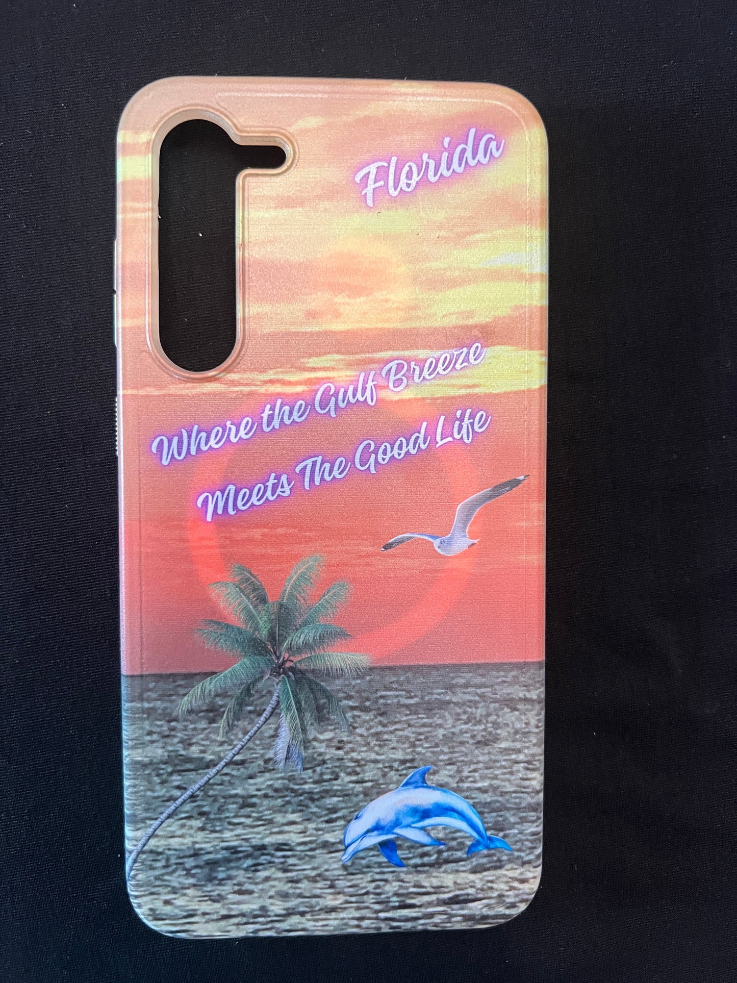 Phone case with Florida design featuring palm tree, dolphin jumping out of the water, seagull jumping out of the gulf water, beautiful Florida sunset, and text with the phrase "where the gulf breeze meets the good like" Florida