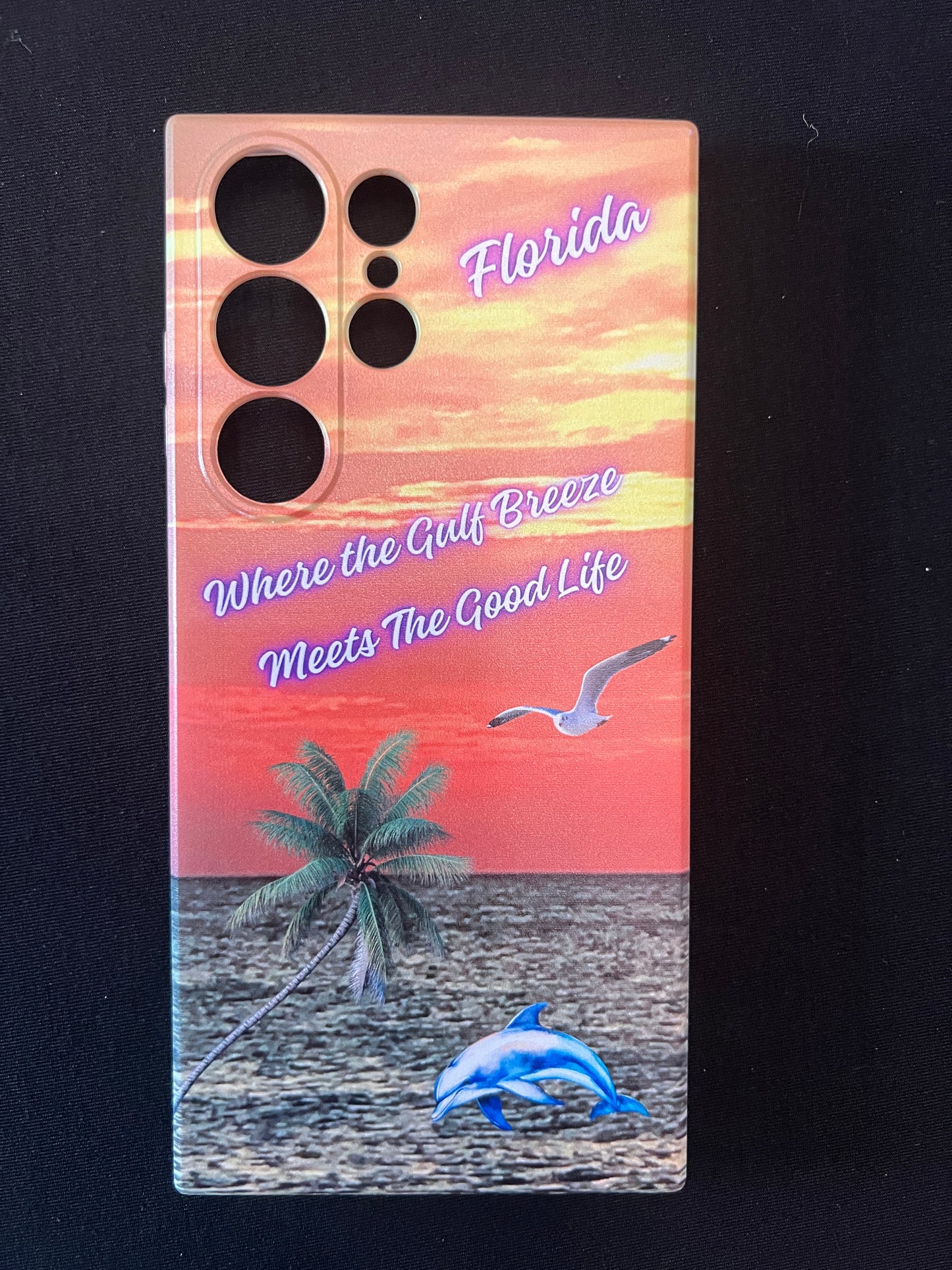 Phone case with Florida design featuring palm tree, dolphin jumping out of the water, seagull jumping out of the gulf water, beautiful Florida sunset, and text with the phrase "where the gulf breeze meets the good like" Florida