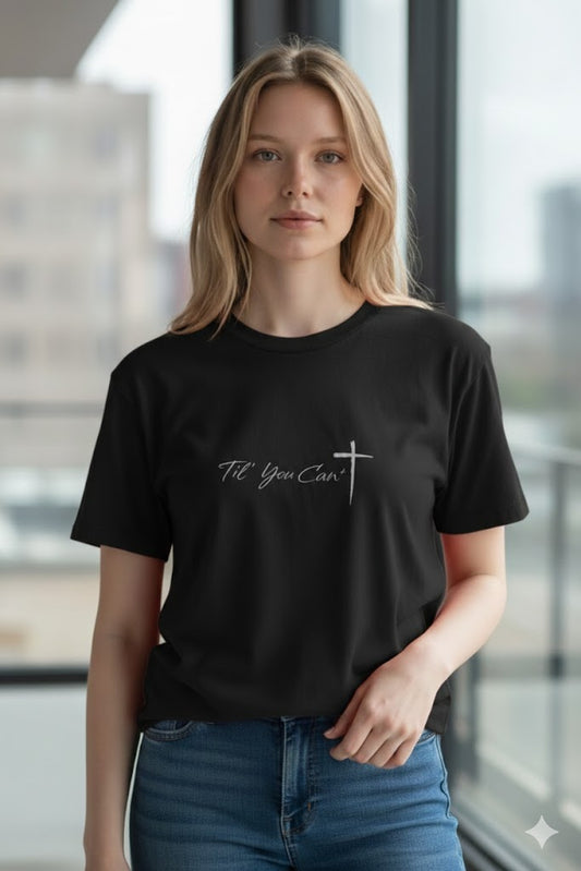 Person wearing a black t-shirt with text and a cross design in an indoor setting