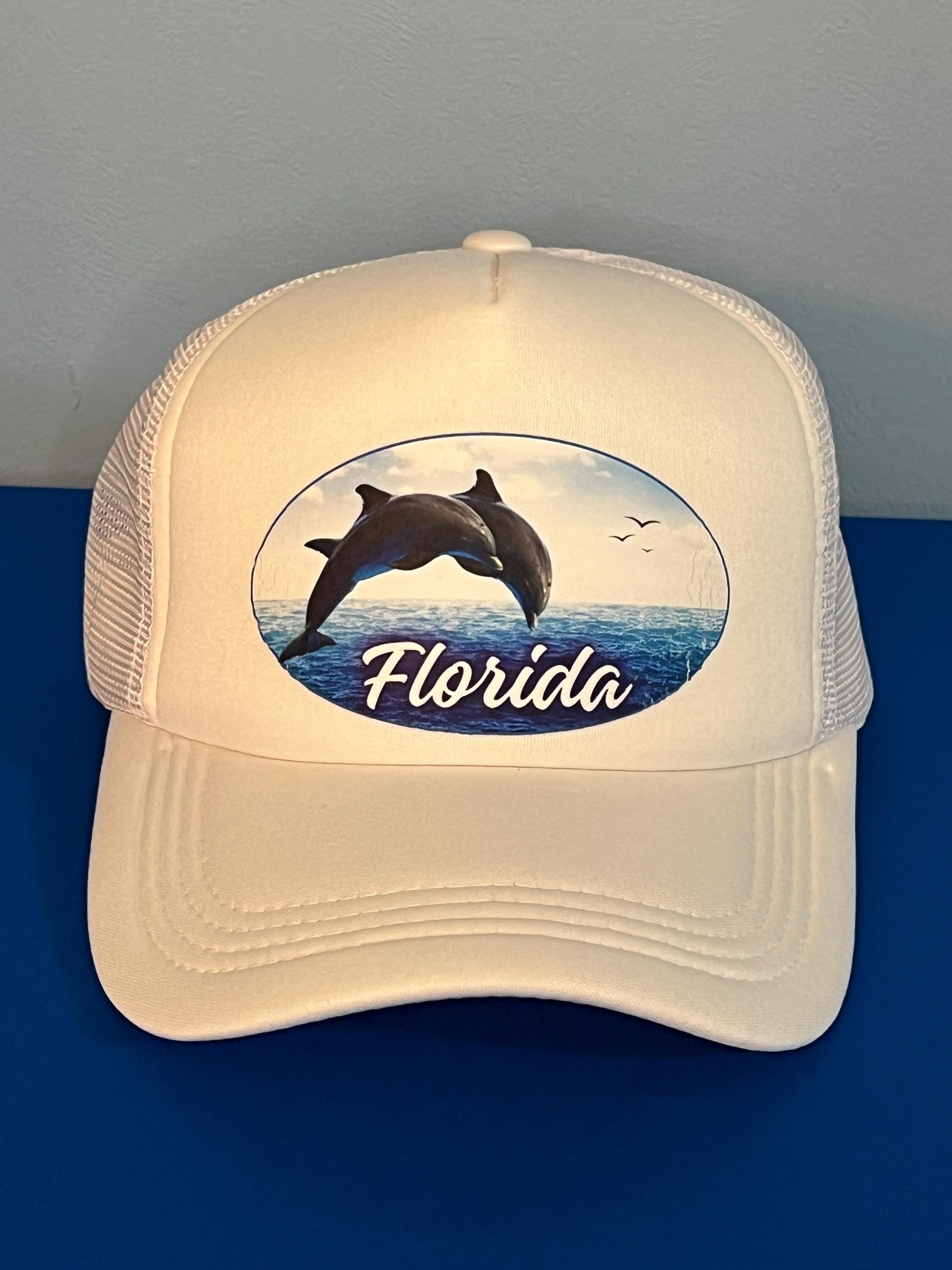White cap with dolphin design and 'Florida' text on a blue gulf water