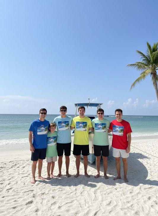 Group of six people standing on a sandy beach with a clear blue sky and ocean in the background.