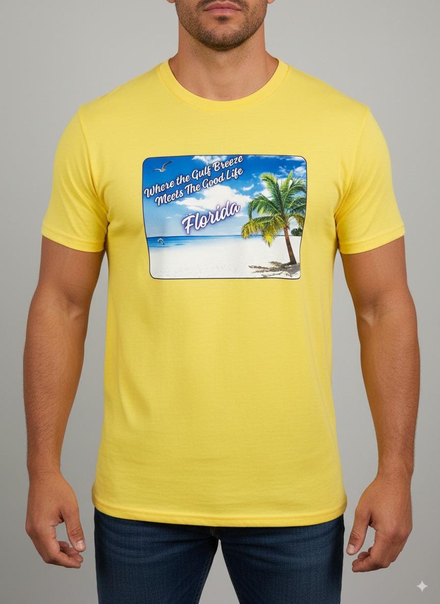 Person wearing a yellow 'Florida' t-shirt on a beach with a sailboat and palm trees in the background. T-shirt has a  picture on the front of white sand beach, aqua gulf waters, palm tree and the text "where the gulf breeze meets the good life" Florida. 