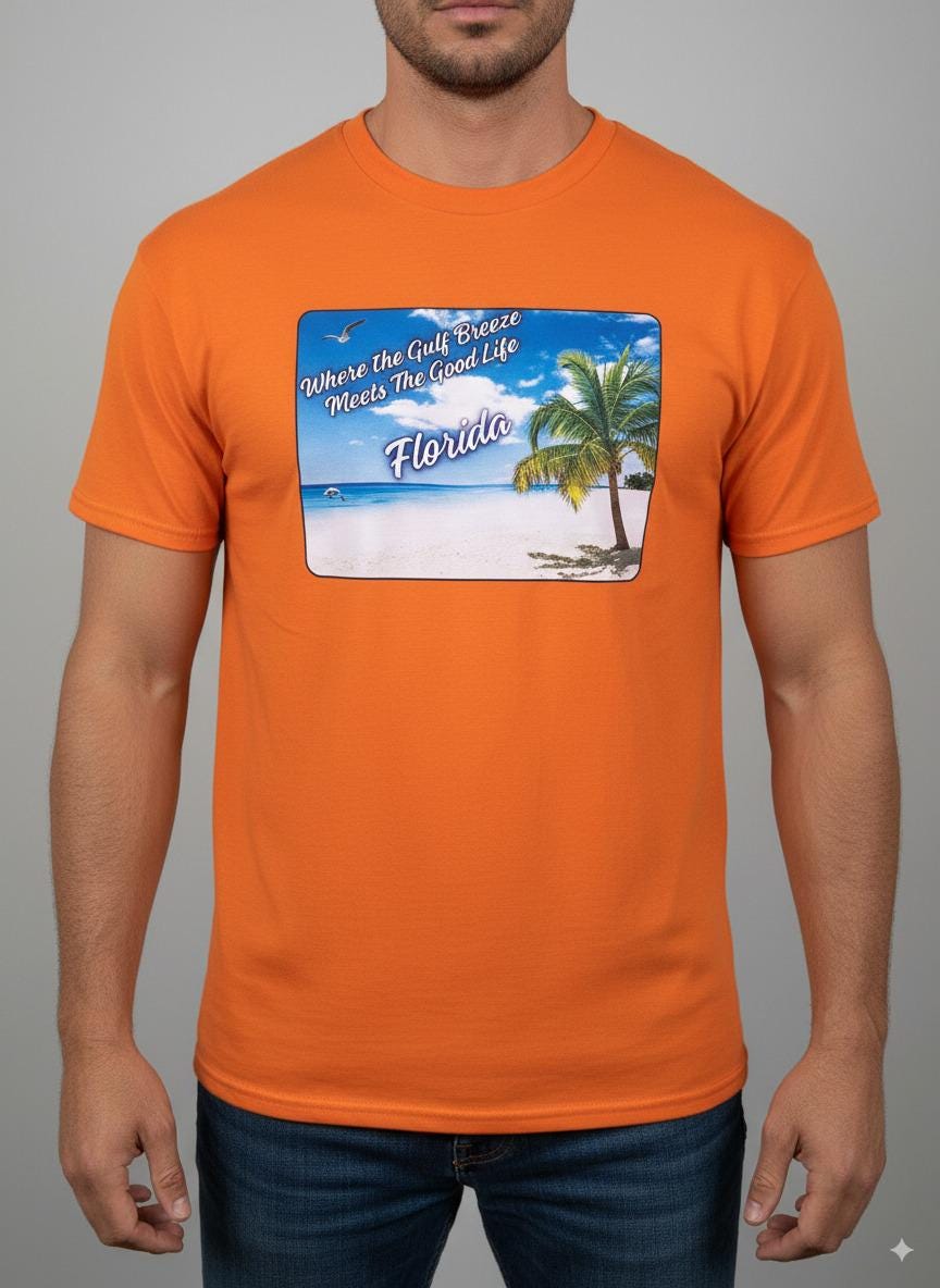 Person wearing a orange 'Florida' t-shirt on a beach with a sailboat and palm trees in the background. T-shirt has a  picture on the front of white sand beach, aqua gulf waters, palm tree and the text "where the gulf breeze meets the good life" Florida. 