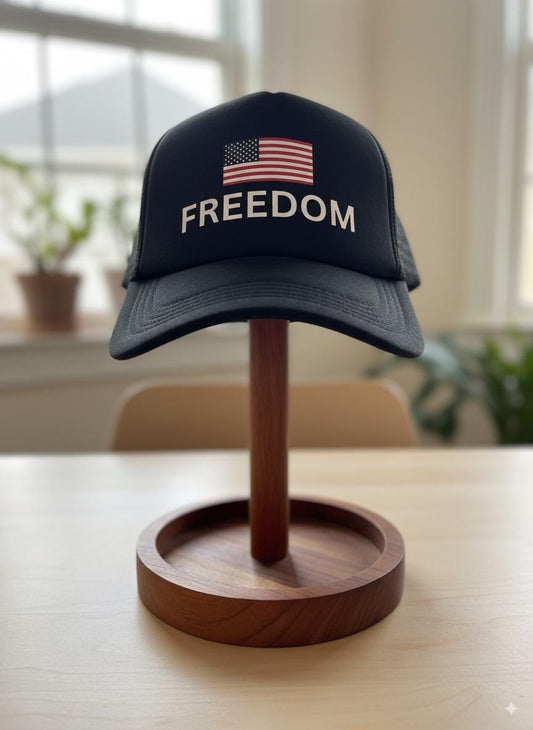 Black cap with 'FREEDOM' and American flag on a wooden stand indoors.
