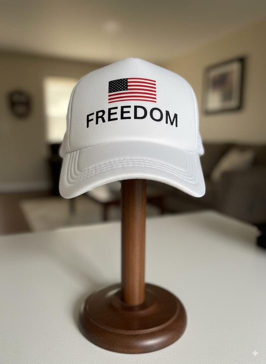 White cap with 'FREEDOM' and American flag on a wooden stand in a room setting.