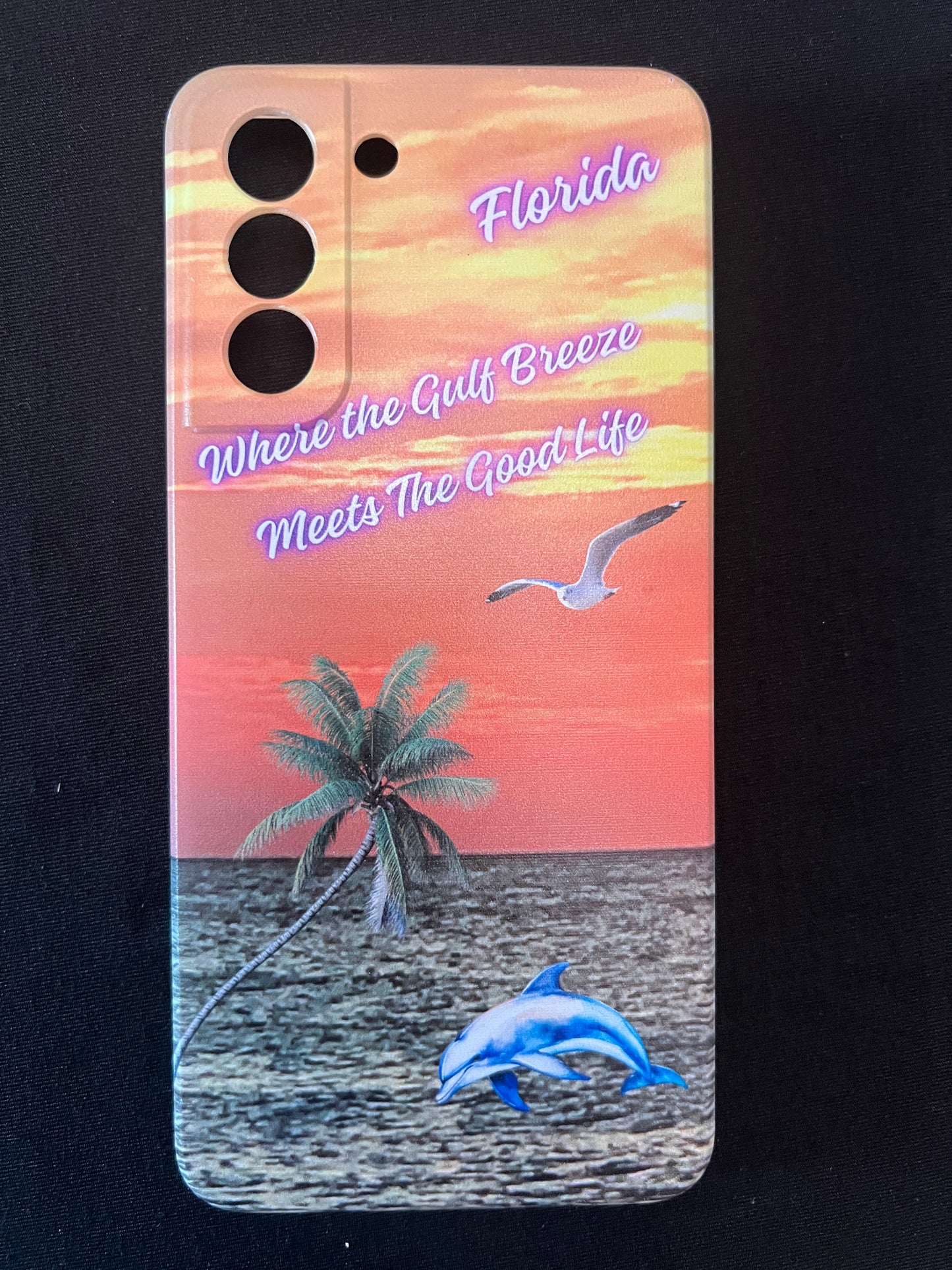 Phone case with Florida design featuring palm tree, dolphin jumping out of the water, seagull jumping out of the gulf water, beautiful Florida sunset, and text with the phrase "where the gulf breeze meets the good like" Florida